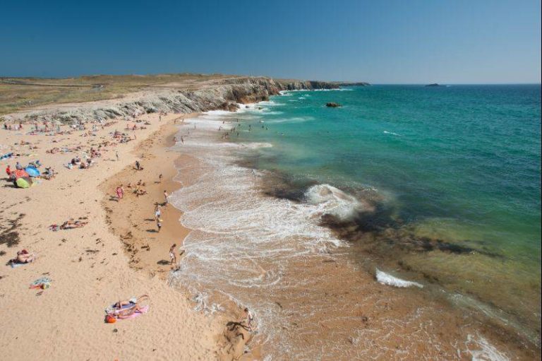 Plage ensoleillée avec mer turquoise et rochers.